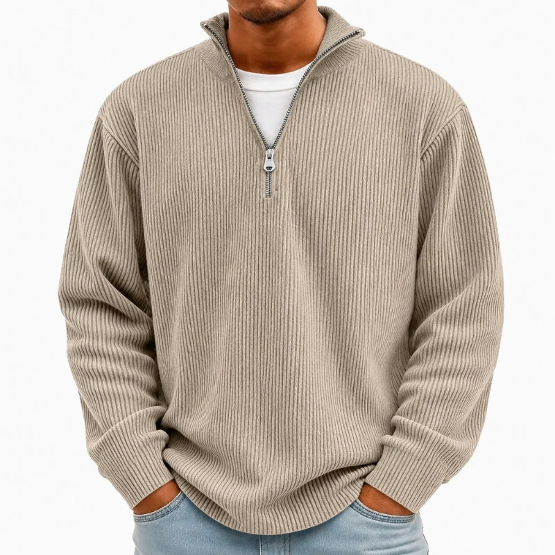 A man wearing a beige ribbed quarter-zip pullover sweater over a white t-shirt and light blue jeans, shown from the neck down against a plain white background.