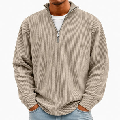 A man wearing a beige ribbed quarter-zip pullover sweater over a white t-shirt and light blue jeans, shown from the neck down against a plain white background.