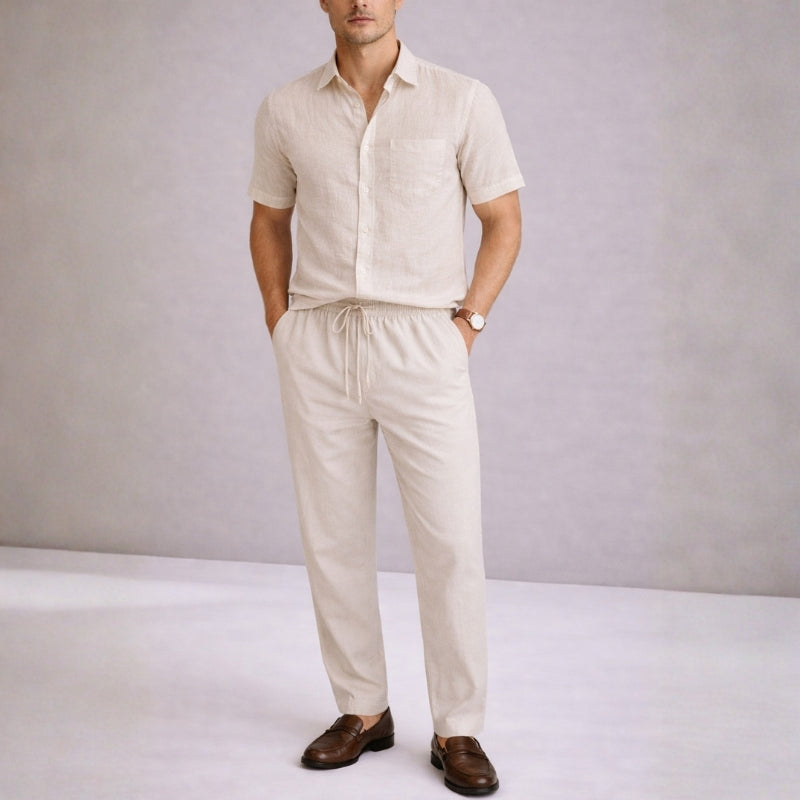 Man wearing a khaki linen shirt and pants with brown shoes on a plain background