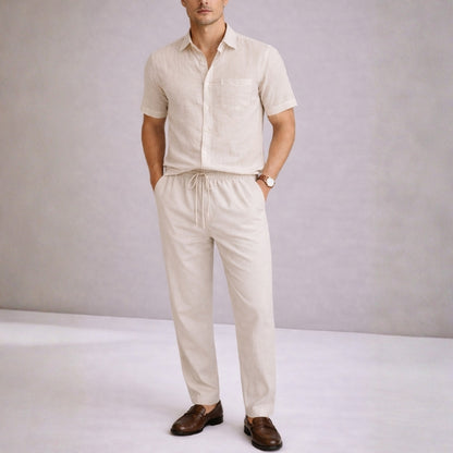 Man wearing a khaki linen shirt and pants with brown shoes on a plain background