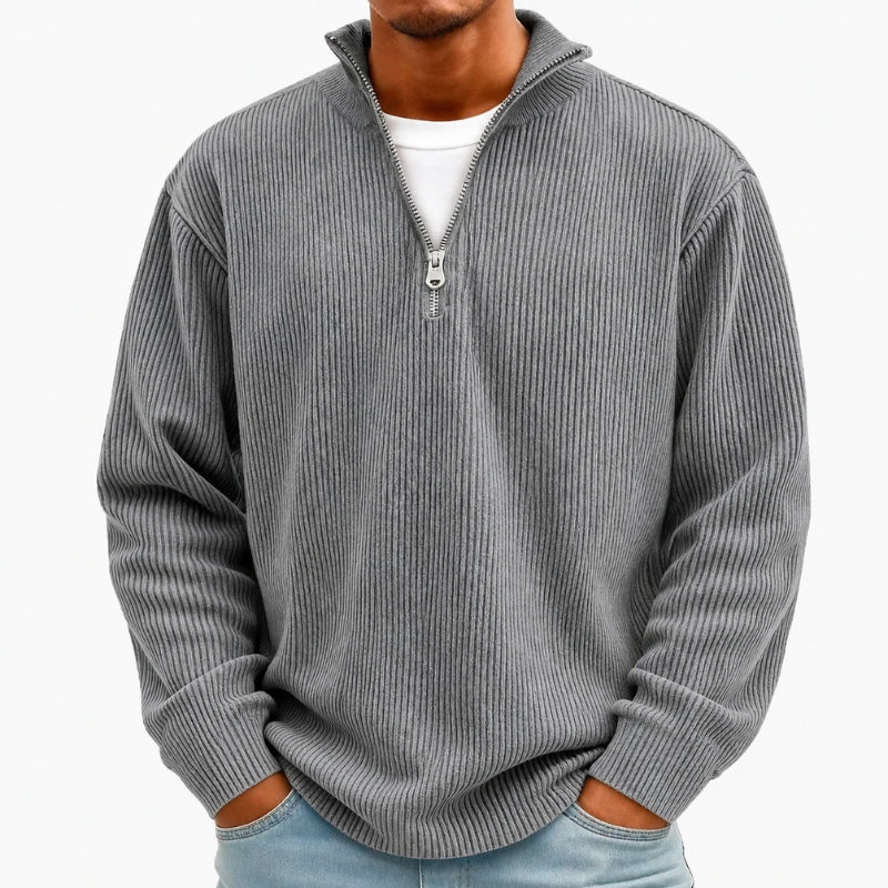 A man wearing a gray ribbed quarter-zip pullover sweater over a white t-shirt and light blue jeans, shown from the neck down against a plain white background.