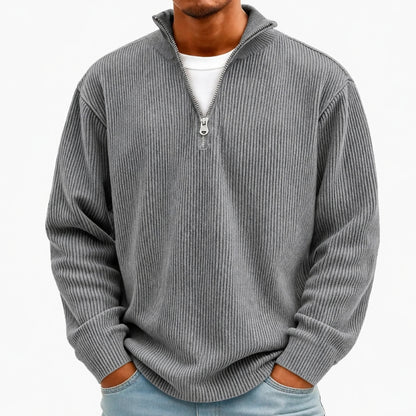 A man wearing a gray ribbed quarter-zip pullover sweater over a white t-shirt and light blue jeans, shown from the neck down against a plain white background.