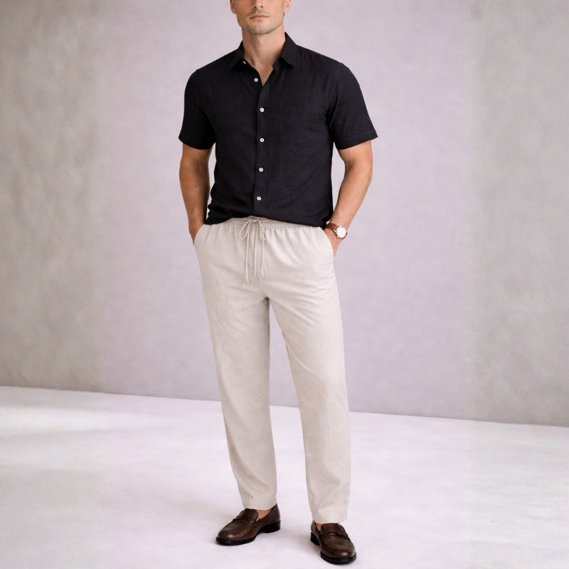 Man wearing a black shirt and beige pants against a plain background