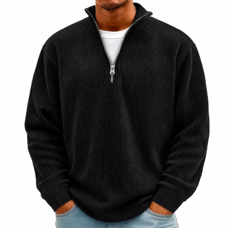 A man wearing a black ribbed knit quarter-zip pullover sweater over a white t-shirt and light blue jeans, shown from the chin down against a plain white background.