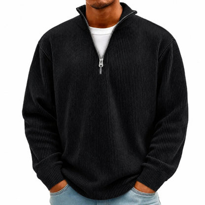 A man wearing a black ribbed knit quarter-zip pullover sweater over a white t-shirt and light blue jeans, shown from the chin down against a plain white background.