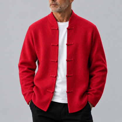 A man wearing a bright red traditional Chinese-style jacket with frog closures over a white t-shirt and black pants, photographed against a neutral gray background.