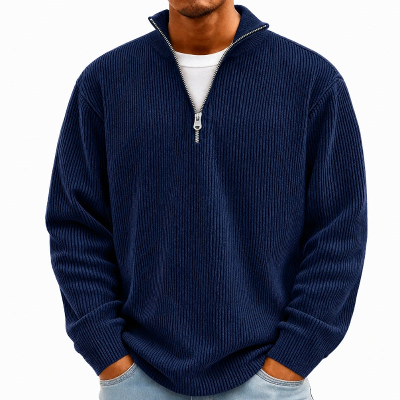 A man wearing a navy blue ribbed knit quarter-zip sweater over a white t-shirt and light blue jeans, shown from the chin down against a plain white background.