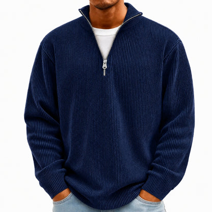 A man wearing a navy blue ribbed knit quarter-zip sweater over a white t-shirt and light blue jeans, shown from the chin down against a plain white background.