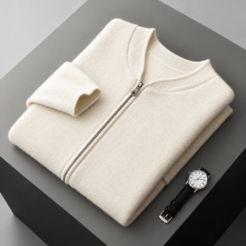 A folded cream-colored zip-up sweater is displayed on a dark gray geometric surface next to a black leather strap wristwatch.