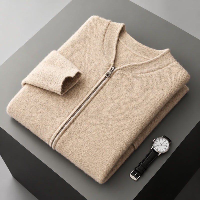A folded beige zip-up sweater with a stand collar and ribbed cuffs, displayed on a dark gray geometric surface next to a black leather wristwatch.