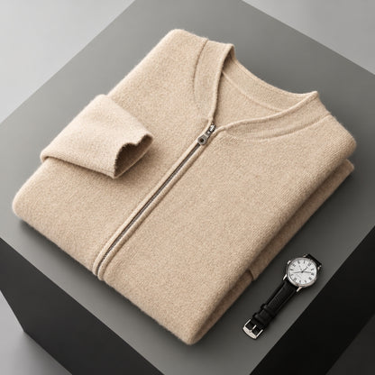 A folded beige zip-up sweater with a stand collar and ribbed cuffs, displayed on a dark gray geometric surface next to a black leather wristwatch.