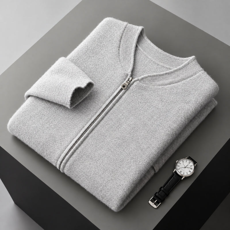 A folded light gray zip-up sweater or lightweight jacket is displayed on a dark gray pedestal, with a wristwatch placed beside it. No person, animal, or real environment is present, so this is Product/Packaging rather than Lifestyle.
