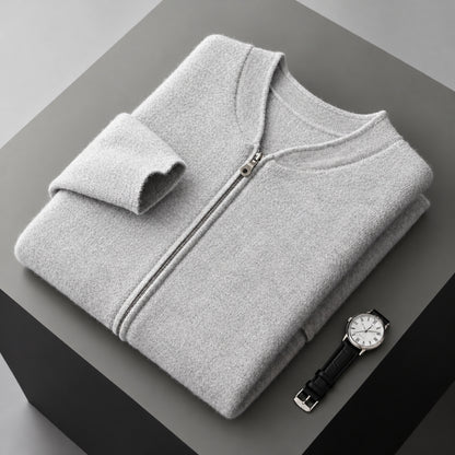 A folded light gray zip-up sweater or lightweight jacket is displayed on a dark gray pedestal, with a wristwatch placed beside it. No person, animal, or real environment is present, so this is Product/Packaging rather than Lifestyle.