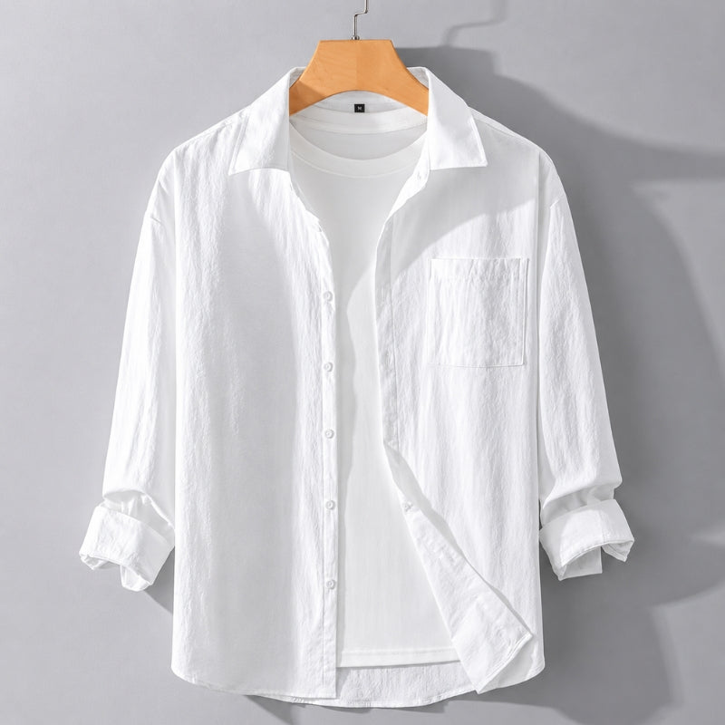 A white long-sleeve button-up shirt with a chest pocket, styled open over a white t-shirt on a wooden hanger against a gray background.
