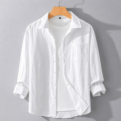 A white long-sleeve button-up shirt with a chest pocket, styled open over a white t-shirt on a wooden hanger against a gray background.