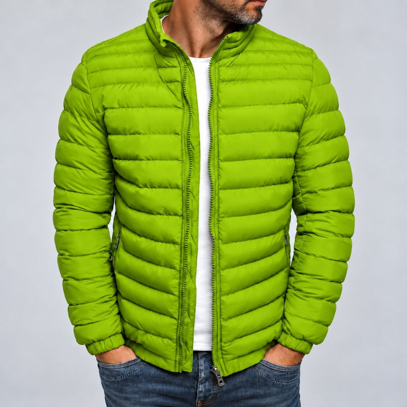 A man wearing a bright lime green puffer jacket over a white t-shirt and blue jeans, shown from the chin down against a light gray studio background.