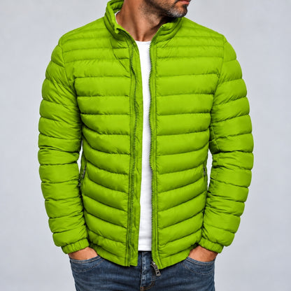 A man wearing a bright lime green puffer jacket over a white t-shirt and blue jeans, shown from the chin down against a light gray studio background.