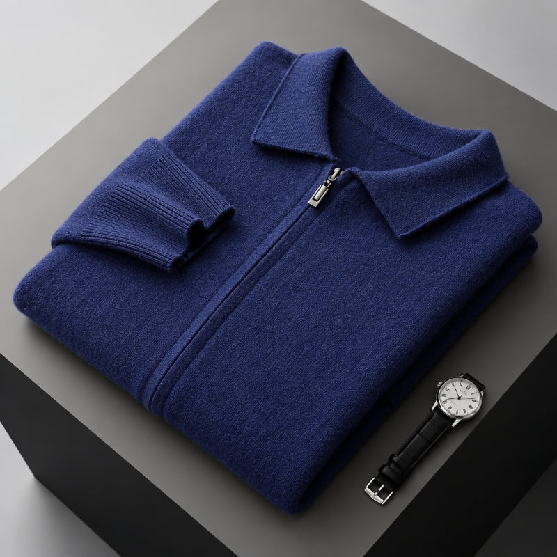 A folded navy blue knit zip-up sweater with a collar and ribbed cuffs, displayed on a dark gray pedestal next to a black leather wristwatch.