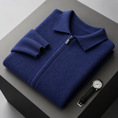 A folded navy blue knit zip-up sweater with a collar and ribbed cuffs, displayed on a dark gray pedestal next to a black leather wristwatch.