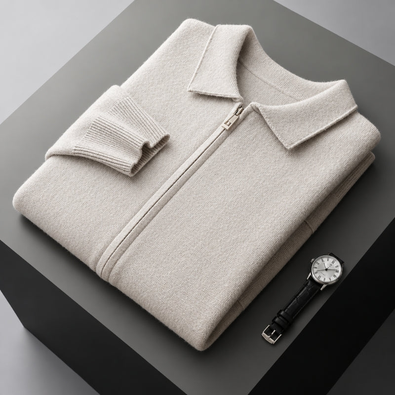 A folded light beige zip-up sweater with a collar and ribbed sleeve cuff, displayed on a dark gray geometric pedestal next to a black leather strap wristwatch.