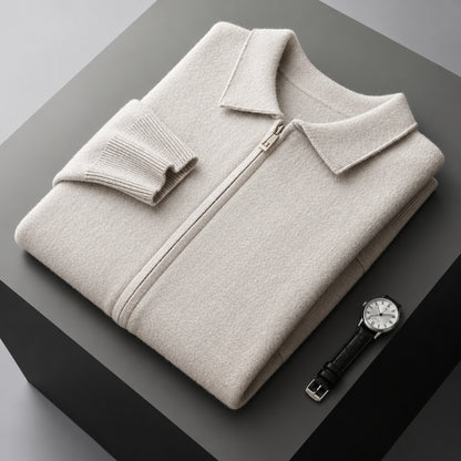 A folded light beige zip-up sweater with a collar and ribbed sleeve cuff, displayed on a dark gray geometric pedestal next to a black leather strap wristwatch.