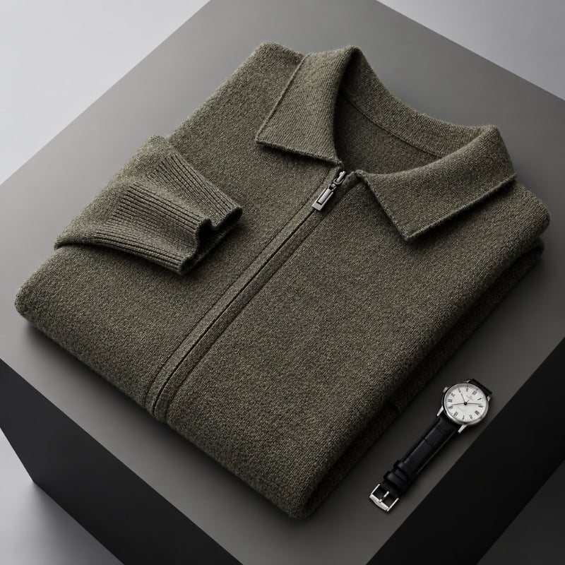 An olive green knit zip-up sweater with a pointed collar and folded cuff, displayed on a dark gray geometric platform next to a black leather watch.