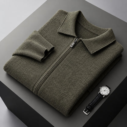 An olive green knit zip-up sweater with a pointed collar and folded cuff, displayed on a dark gray geometric platform next to a black leather watch.