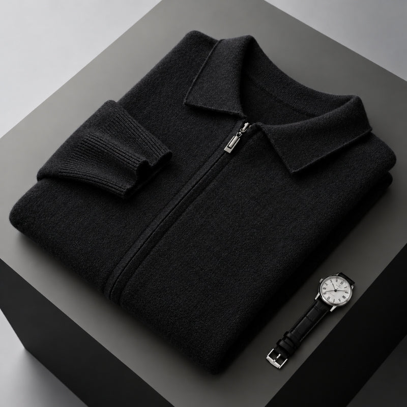 A folded black knit zip-up sweater with a collar and ribbed cuffs, displayed on a dark gray pedestal alongside a black leather wristwatch.