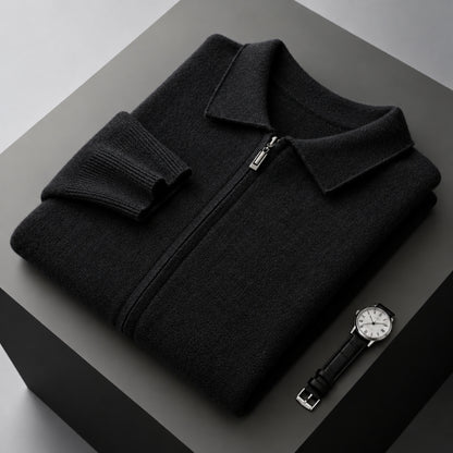A folded black knit zip-up sweater with a collar and ribbed cuffs, displayed on a dark gray pedestal alongside a black leather wristwatch.