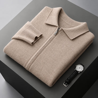 A folded beige knit zip-up sweater with a collar and ribbed cuffs, displayed on a dark gray pedestal alongside a wristwatch.