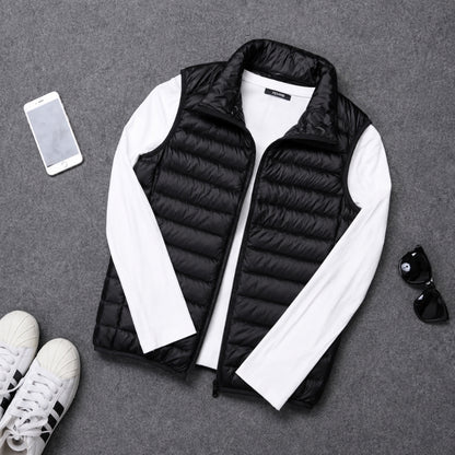 A black quilted puffer vest styled in a flat lay with a white long-sleeve shirt underneath, accompanied by a smartphone, sunglasses, and sneakers on a gray textured background.