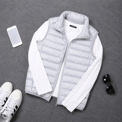 A light gray puffer vest layered over a white long-sleeve shirt, arranged in a flat lay on a gray textured surface with a smartphone, white sneakers, and black sunglasses nearby.