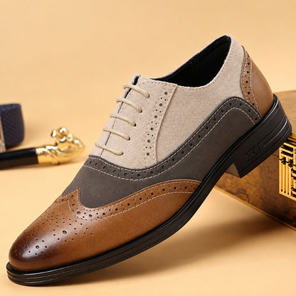 A men's three-tone wingtip oxford shoe with a brown brogue toe, a medium brown suede side panel, and a light beige suede quarter, resting on a gold-toned box against a beige background.