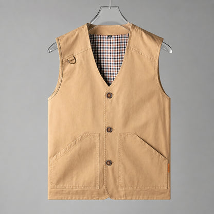 A tan canvas utility vest with a V-neck, three button closures, and two large front patch pockets, hanging on a clear plastic hanger against a solid gray background.