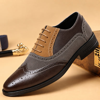 A men's wingtip oxford shoe with a color-blocked design featuring dark brown leather, medium brown suede, and dark gray panels, shown on a beige background with decorative props.