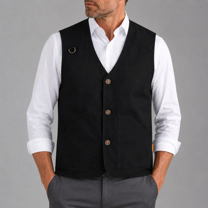 A man wearing a black waistcoat vest over a white collared shirt and gray trousers, shown from the lower face to the upper thighs against a plain gray studio background.