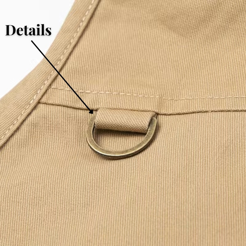 Close-up detail shot of a beige canvas garment featuring a brass D-ring hanging from a reinforced eyelet tab, with a text overlay pointing to the details.