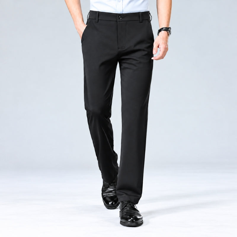 A model from the waist down wearing black slim-fit dress pants, a white shirt, and black dress shoes, walking against a light gray studio background.