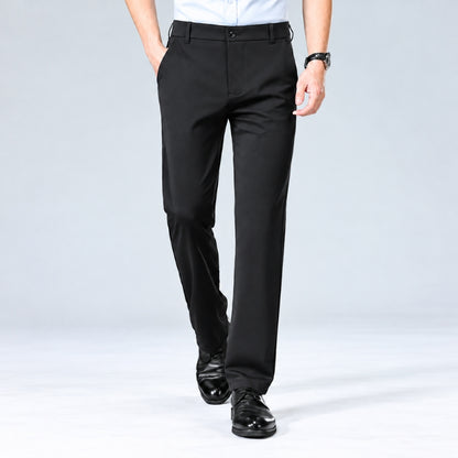 A model from the waist down wearing black slim-fit dress pants, a white shirt, and black dress shoes, walking against a light gray studio background.