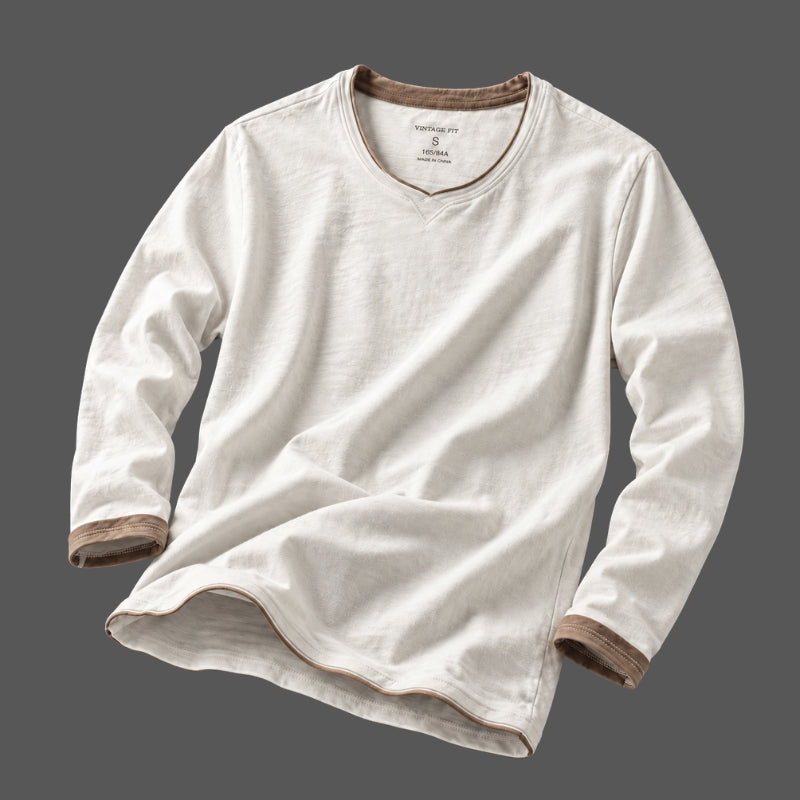 A long-sleeve V-neck shirt in off-white cotton-linen fabric, featuring brown ribbed trim along the collar, cuffs, and hem, displayed against a solid dark gray background.