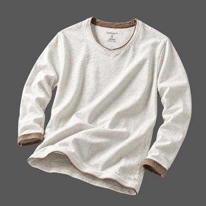 A long-sleeve V-neck shirt in off-white cotton-linen fabric, featuring brown ribbed trim along the collar, cuffs, and hem, displayed against a solid dark gray background.