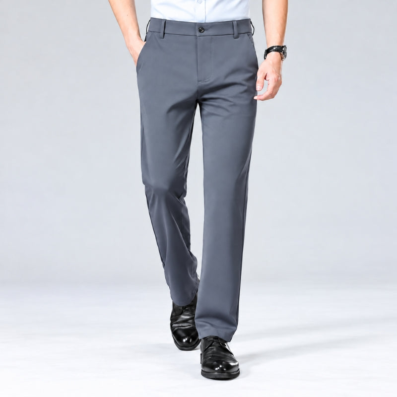 A person wearing gray dress pants with a white shirt and black dress shoes, shown from the waist down against a light gray studio background.