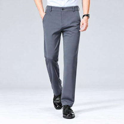 A person wearing gray dress pants with a white shirt and black dress shoes, shown from the waist down against a light gray studio background.