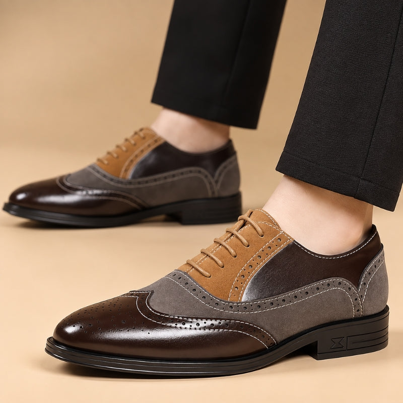 A pair of men's three-tone wingtip oxford shoes worn with black trousers, shown against a solid beige background. The shoes feature a dark brown leather toe, a medium brown leather vamp, and a gray suede overlay with tan wingtip and lace sections.