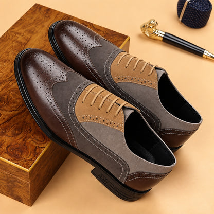A pair of men's wingtip oxford shoes in dark brown and taupe suede, displayed on a wooden box with a gold pen and a blue pocket square on a beige background.