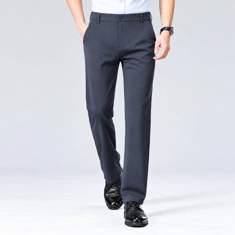 A person wearing dark charcoal gray dress pants with a white shirt and black dress shoes, shown from the waist down against a light gray studio background.