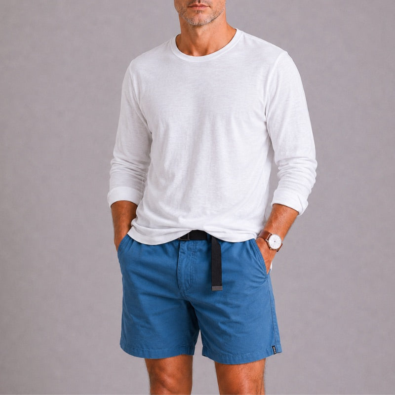 Man wearing a white long-sleeve shirt and blue shorts on a gray background