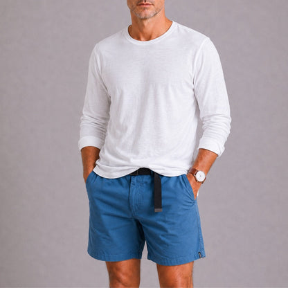 Man wearing a white long-sleeve shirt and blue shorts on a gray background