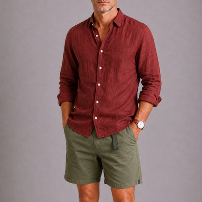 Man wearing a maroon button-up shirt and green shorts against a gray background