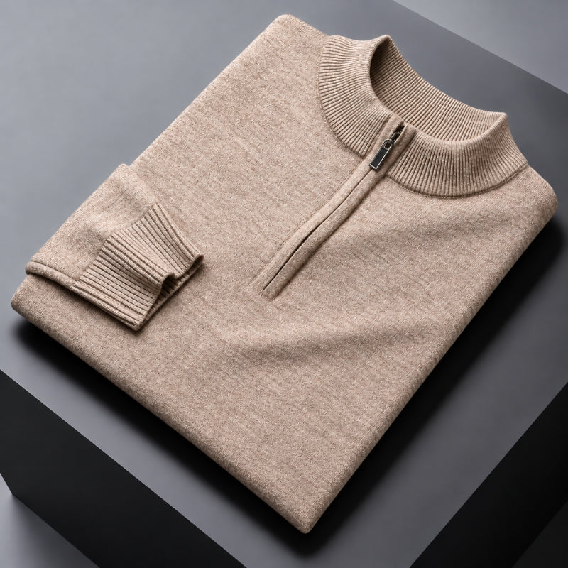 A folded beige knit quarter-zip sweater with a ribbed mock neck and sleeve cuff, displayed on a dark gray surface.